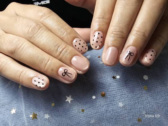 Nude nails with black polka dots and a bow design